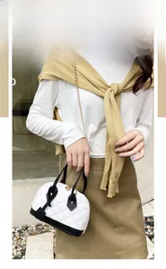 Détail du sac coquille blanc matelassé avec bordure noire et chaîne dorée