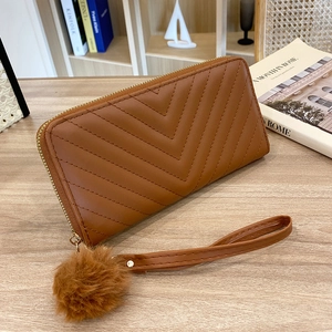 Brown quilted V-pattern long wallet with wristlet and plush ball charm on wooden desk