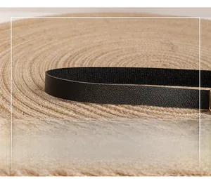 Detail of black pebbled leather shoulder strap with a gold metal clasp on woven mat