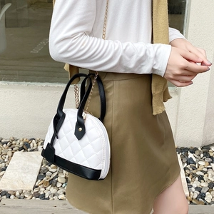 Sac coquille bicolore à motif losanges avec chaîne dorée porté par un mannequin dehors