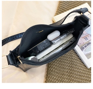 Detailed interior of black croc-effect underarm bag holding phone and cosmetics