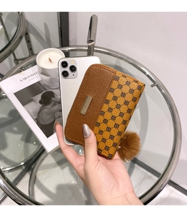 Portafoglio compatto patchwork con stampa floreale e pompon accanto a uno smartphone