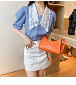 Detail view of orange crocodile pattern faux leather underarm bag with gold metal accents