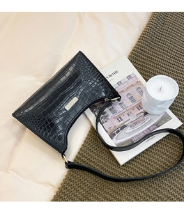 Close-up of black crocodile-embossed shoulder bag with gold metal plaque on bedding