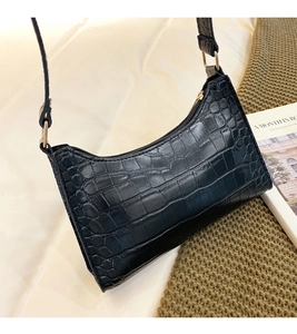 Close-up of black faux crocodile leather texture and golden metal buckle on shoulder bag