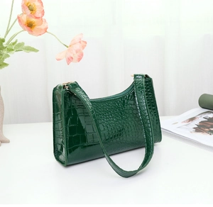 Detail view of deep green crocodile texture underarm bag with gold zipper and strap