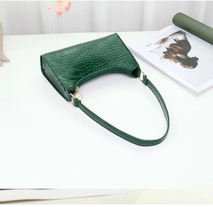 Detailed texture of dark green crocodile embossed underarm bag with gold metal zipper