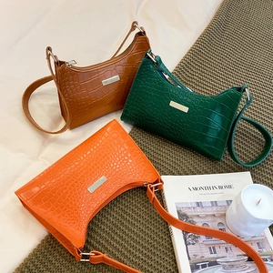 Three crocodile texture underarm bags in orange, green, and brown on a soft bed setting