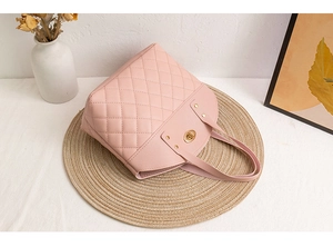 Detailed view of pink quilted handbag with golden oval twist lock on a woven mat