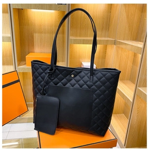 Close-up of black quilted tote bag with matching zippered pouch on an orange gift box