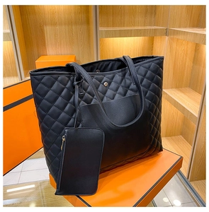 Detail of black quilted tote bag with matching pouch on a vibrant orange pedestal