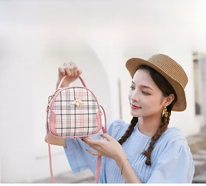 Outdoor model display of a pink plaid handbag with a golden bee clasp and thin strap