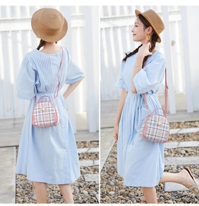 Outdoor view of a pink plaid crossbody bag with a gold bee ornament on a blue dress