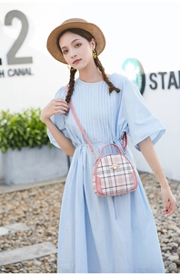 Detail of pink plaid crossbody bag with gold bee ornament held by model in blue dress