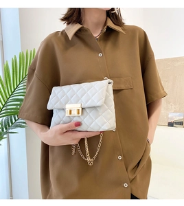 Close-up of a white quilted crossbody bag with gold buckle and chain strap on a model