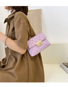 Detail view of purple quilted shoulder bag with gold chain strap worn by a model