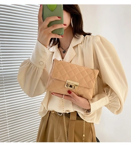 Detail shot of beige quilted crossbody bag with gold metal square lock and chain strap
