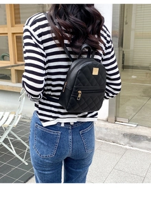 Detail of classic black quilted mini backpack with golden metal zippers on street