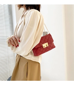 Close-up of deep red quilted leather shoulder bag with gold chain strap on a model