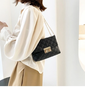 Detail of a black quilted crossbody bag with a gold rectangular lock and chain strap