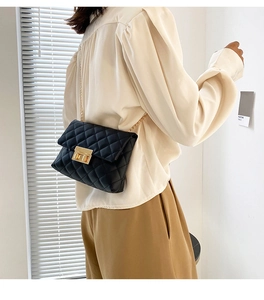 Detail of a black quilted crossbody bag with a gold chain strap and metal lock closure