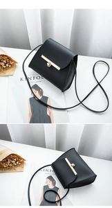 Detail of minimalist black leather crossbody bag with gold metal bar and round lock