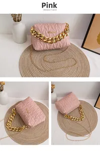 Detail of pink quilted handbag with gold chain straps and metallic logo on white surface
