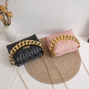 Black and pink quilted shoulder bags with gold chain handles on a woven mat
