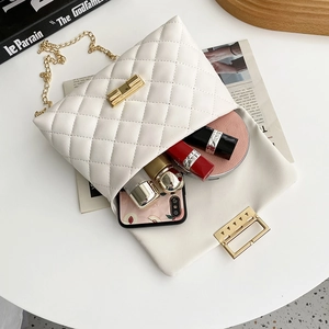 White quilted crossbody bag with gold chain strap and turn-lock closure on lifestyle background