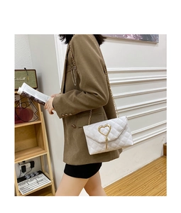 Model wearing a white quilted crossbody bag with a gold heart clasp and chain strap