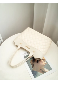 Détail du sac cabas matelassé crème avec logo doré sur une table blanche épurée