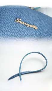 Detail of blue pebble leather handbag featuring a gold Serenity logo and stitched strap