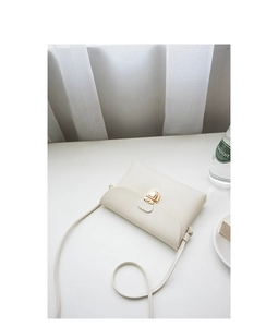 Detail of cream white crossbody bag featuring lychee texture and gold round lock closure