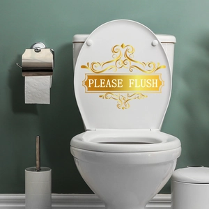 Detail eines goldenen 'PLEASE FLUSH' Aufklebers auf einem weißen Toilettendeckel im Bad