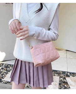 Détail du sac bandoulière rose matelassé avec chaîne dorée porté par un mannequin