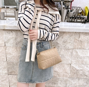 Détail du sac bandoulière matelassé beige avec chaîne dorée dans un café moderne