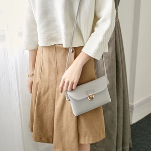 Light grey leather crossbody flap bag with a gold metal lock, styled for casual wear