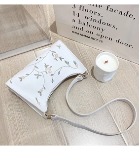 Close-up of elegant floral embroidery on a white PU leather shoulder bag with gold hardware