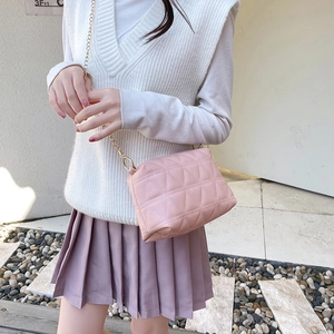 Sac bandoulière matelassé rose pâle avec chaîne dorée porté par un mannequin en extérieur
