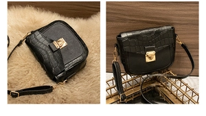 Detail of black crossbody bag with faux crocodile flap and golden metal clasp on wood