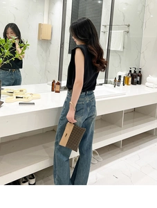 Detail of checkered clutch bag with leather handle held by a model in a modern bathroom