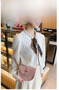 Pink crocodile embossed saddle bag shown on a model in a natural cafe setting