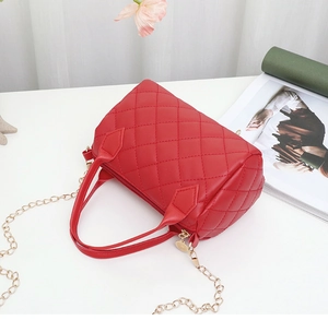 Detailed close-up of a red quilted barrel handbag with golden chain strap on white desk