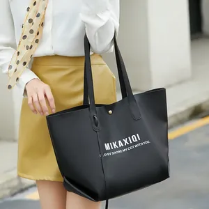 Close-up of a large black leather tote bag with white text held by a stylish model