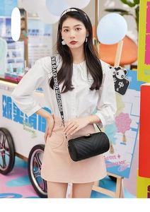 Detail of a black cylinder crossbody bag with V-quilted faux leather and a wide lettered strap