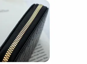 Close-up of black woven leather texture and polished gold zipper with pompom detail