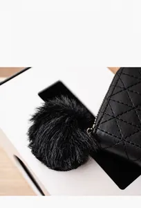 Detail of a fluffy black plush pompom pendant attached to a quilted diamond pattern purse