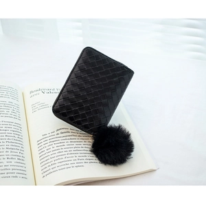 Detailed view of black woven leather wallet with soft fur ball charm on French book