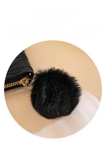 Detail of black faux fur pom-pom charm with gold metal zipper pull on a leather wallet