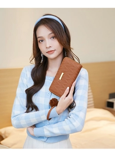 Brown long quilted wallet with gold bar and plush pompom held by model in casual setting